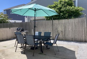 Eine Terrassengruppe mit Tisch und Stühlen, ein grüner Sonnenschirm und ein Holzzaun.