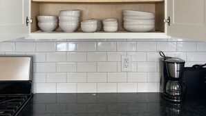 Une cuisine avec des meubles blancs, un plan de travail noir et une machine à café.