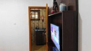 A living room with a TV on a wooden stand, a small statue, and a window with blinds. - Studio C in gated Lekki estate - 5min from a beach (Lekki Phase 1)