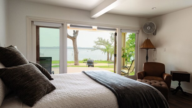 A bedroom with a large bed, a chair, a lamp, and a view of a body of water through a sliding door. - Relaxing Lake Travis waterfront apartment with boat launch (Austin)
