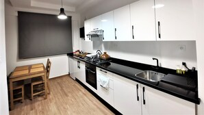 Cozinha moderna com armários brancos, bancada preta e mesa de jantar de madeira.