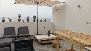Um terraço com mesa, cadeiras, um guarda-sol grande e plantas em vasos.