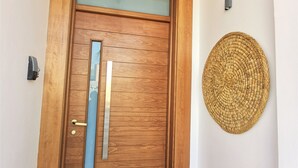 Uma porta de madeira com painel de vidro jateado, puxador vertical de metal e tapete de boas-vindas na entrada.