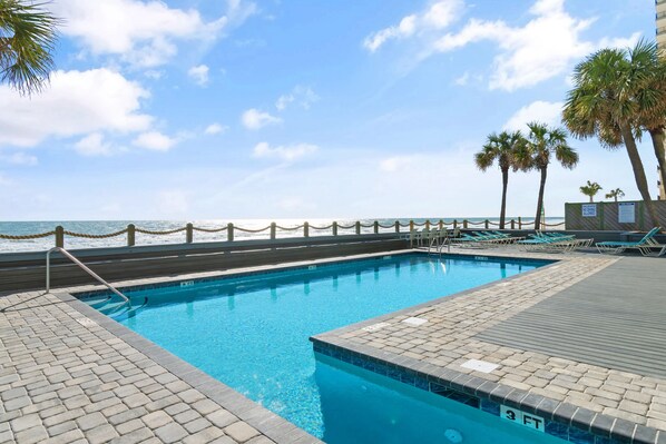 A swimming pool with a wooden deck, a lifeguard stand, and a view of the ocean. - Garden City Beach Oceanfront Condo 1202 | Rising Tides Properties Rental (Murrells Inlet)