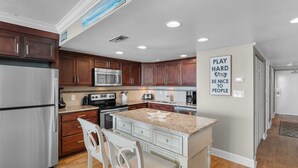 A modern kitchen with wooden cabinets, stainless steel appliances, and a granite countertop island. - Garden City Beach Oceanfront Condo 1202 | Rising Tides Properties Rental (Murrells Inlet)