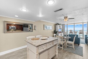 A modern kitchen with a central island, a dining area with a view, and a ceiling fan.