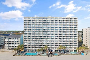A multi-story hotel with balconies, a pool area, and a beach view.