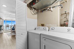 A laundry area with two white Amana washers, a water heater, and a view of the outside.