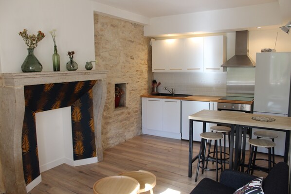 A modern kitchen with white cabinets, a stone accent wall, a fireplace, and a dining area with stools.