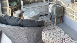 A stone wall interior with a white bench, a wicker chair, and a small table. - Cottage Philmaries (Sainte-Féréole)