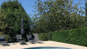 A swimming pool with clear water, surrounded by lounge chairs and a hedge. - Cottage Philmaries (Sainte-Féréole)