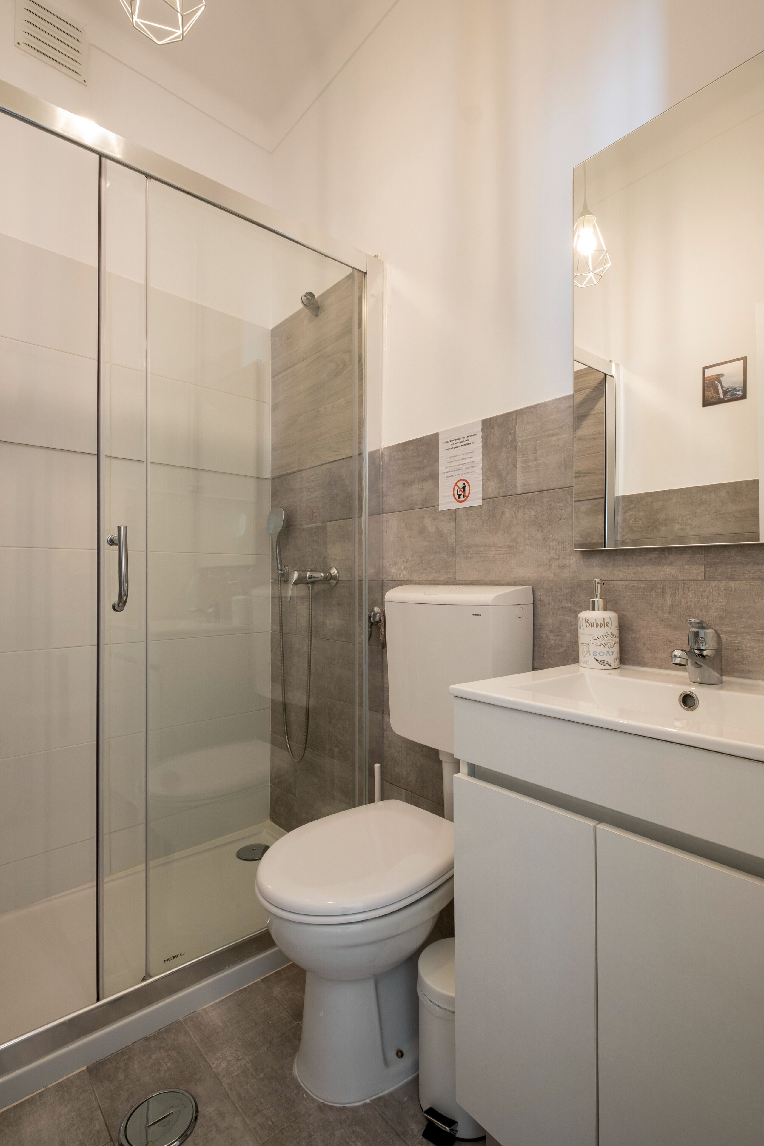 Une salle de bain moderne avec une douche à parois de verre, des toilettes blanches et un lavabo équipé d’un distributeur de savon.