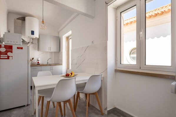 Une cuisine moderne avec des meubles blancs, une table à manger blanche avec des chaises, un four encastré et une fenêtre donnant sur l’extérieur.