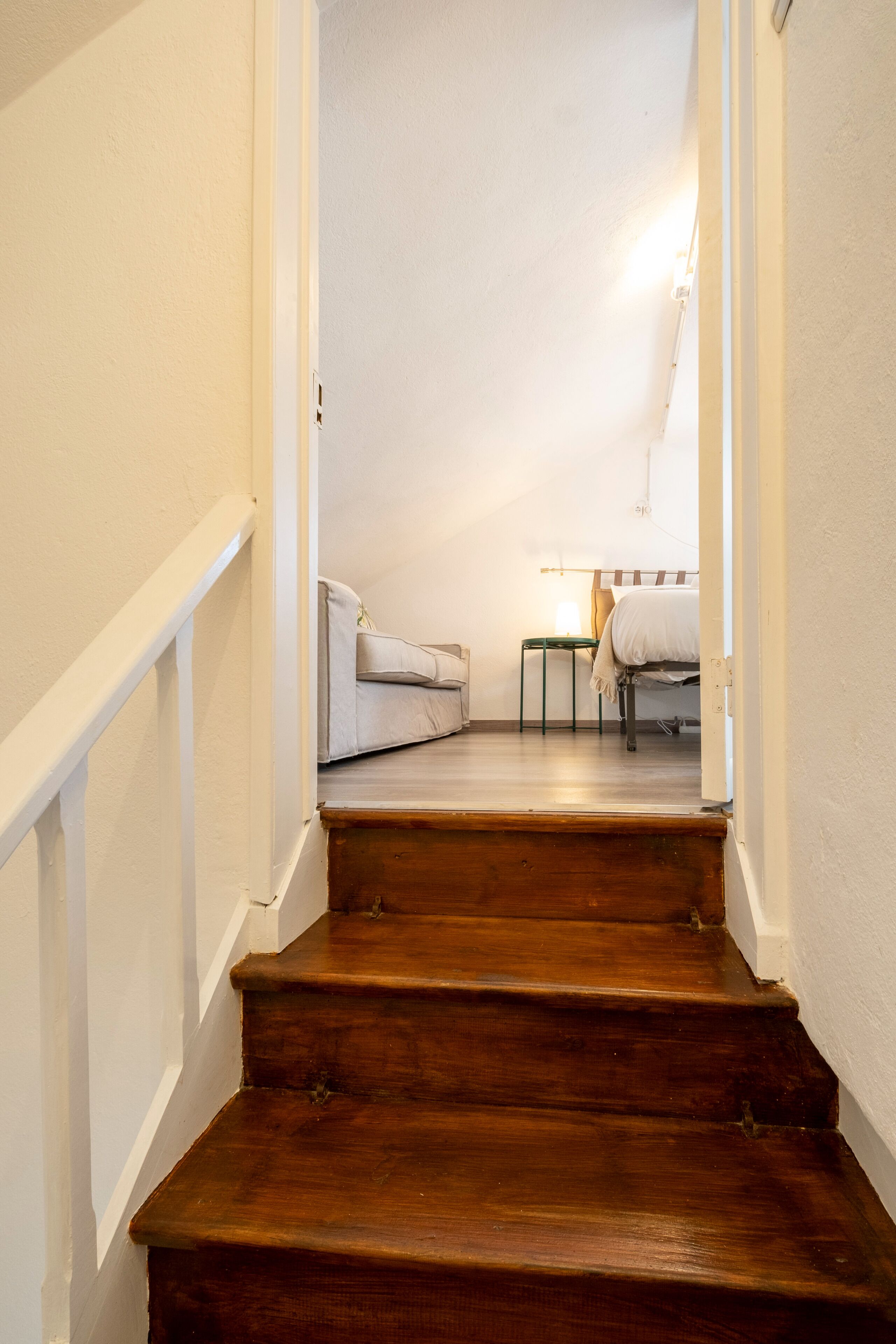 Un escalier en bois mène à une chambre à coucher qui contient un lit, une chaise et une petite table.