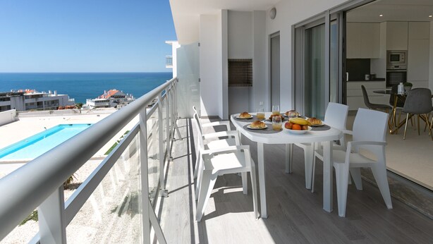 Un balcone con un tavolo da pranzo apparecchiato per la colazione, con vista su una piscina e il mare.