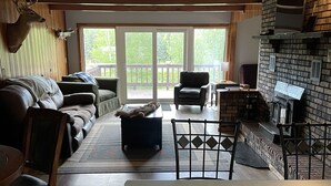 A cozy living room with a fireplace, a dining area, and a view of the outdoors through large sliding glass doors.