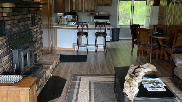 A spacious living area with a fireplace, wooden furniture, and a kitchen in the background.