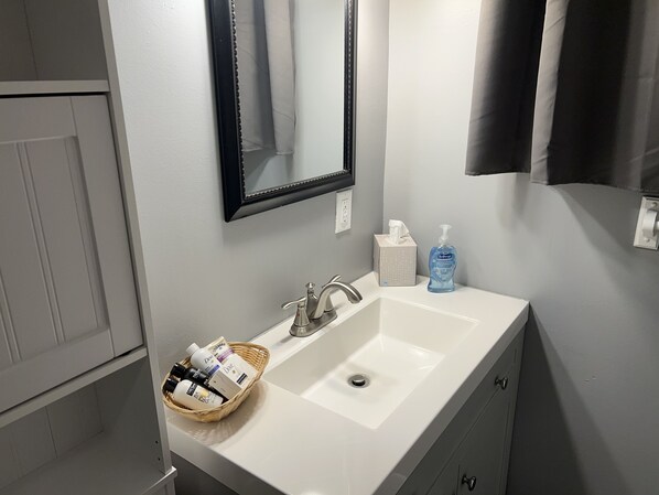 Un baño con un lavamanos blanco, un espejo, una caja de pañuelos y una botella de jabón para manos.