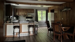 A kitchen with wooden cabinets, a refrigerator, a stove, and a dining area with a table and chairs.
