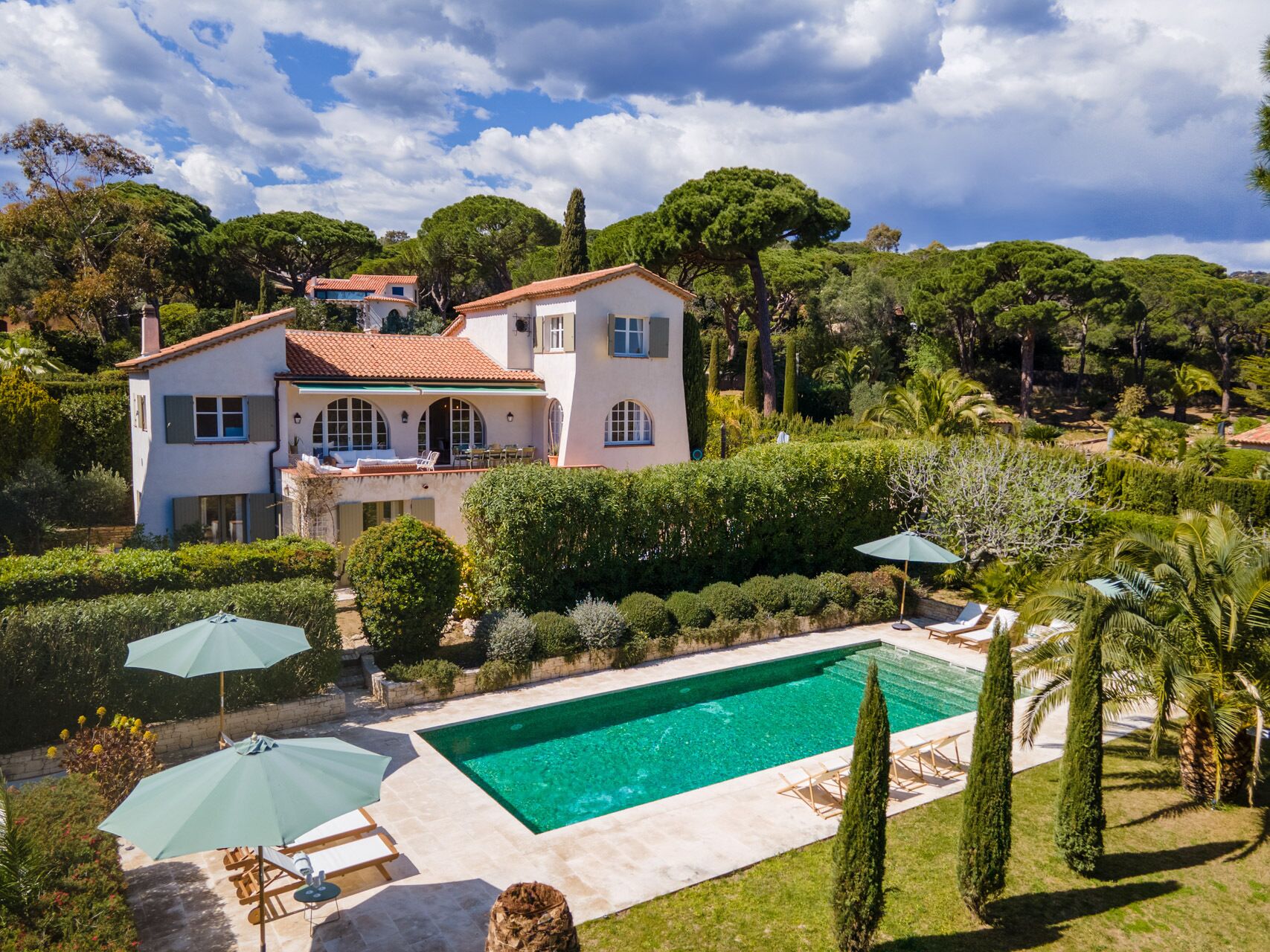 A large house with a swimming pool, surrounded by well-maintained gardens and trees.