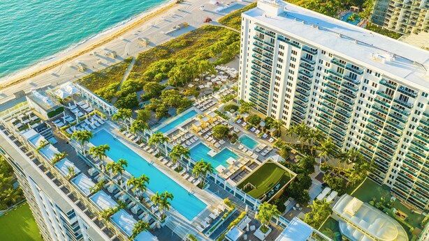 Vista aérea de un complejo turístico con varias piscinas, una playa y edificios altos.