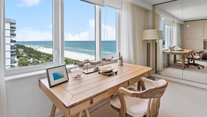 Habitación de hotel con un ventanal grande con vista a una playa, un escritorio de madera con una computadora portátil y una silla.