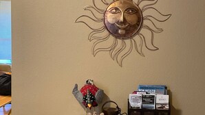 Un mur orné d’un motif solaire décoratif, une petite étagère avec une figurine d’oiseau, une plante et un porte-revues.