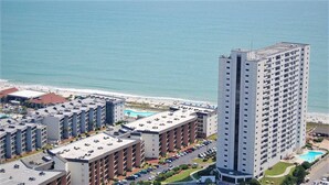 Ett högt hotell med flera våningar, en pool på taket och utsikt över stranden.