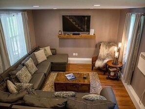 Un salon moderne avec un canapé d’angle, une table basse, un téléviseur fixé au mur et un fauteuil confortable.