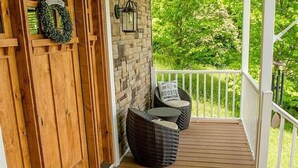Une terrasse en bois avec un muret en pierre, une lanterne et deux fauteuils en osier.