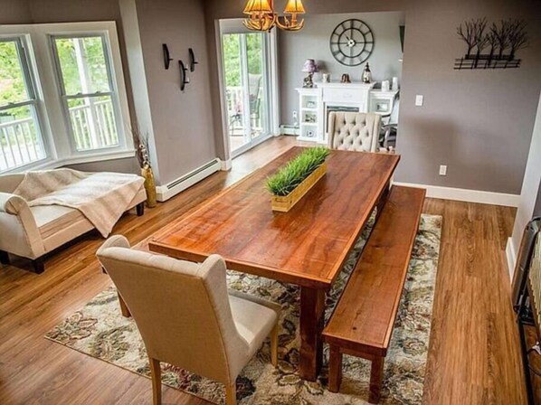 Un coin repas avec une table en bois, des bancs et un tapis. On aperçoit un canapé et un fauteuil au fond.