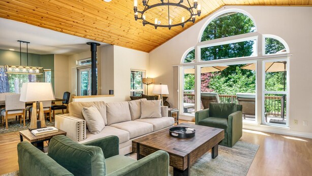 Un salón espacioso con techo alto, vigas de madera, un gran ventanal de arco y una zona de estar acogedora con sofá y sillones.