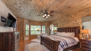 Une chambre dans une cabane en bois, avec un lit, une commode et un ventilateur de plafond.