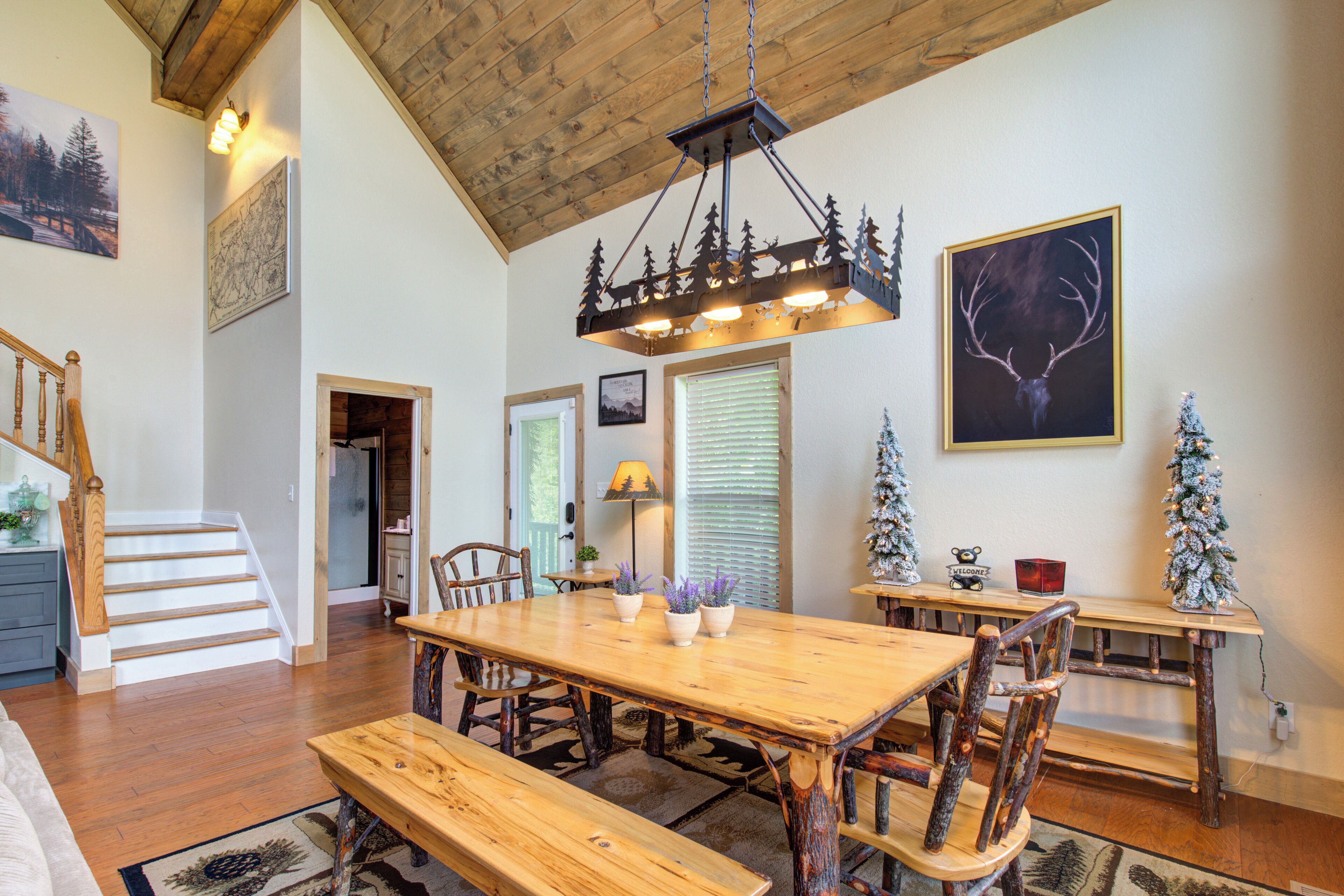 A spacious dining area with a wooden table and benches, a staircase, and a chandelier.