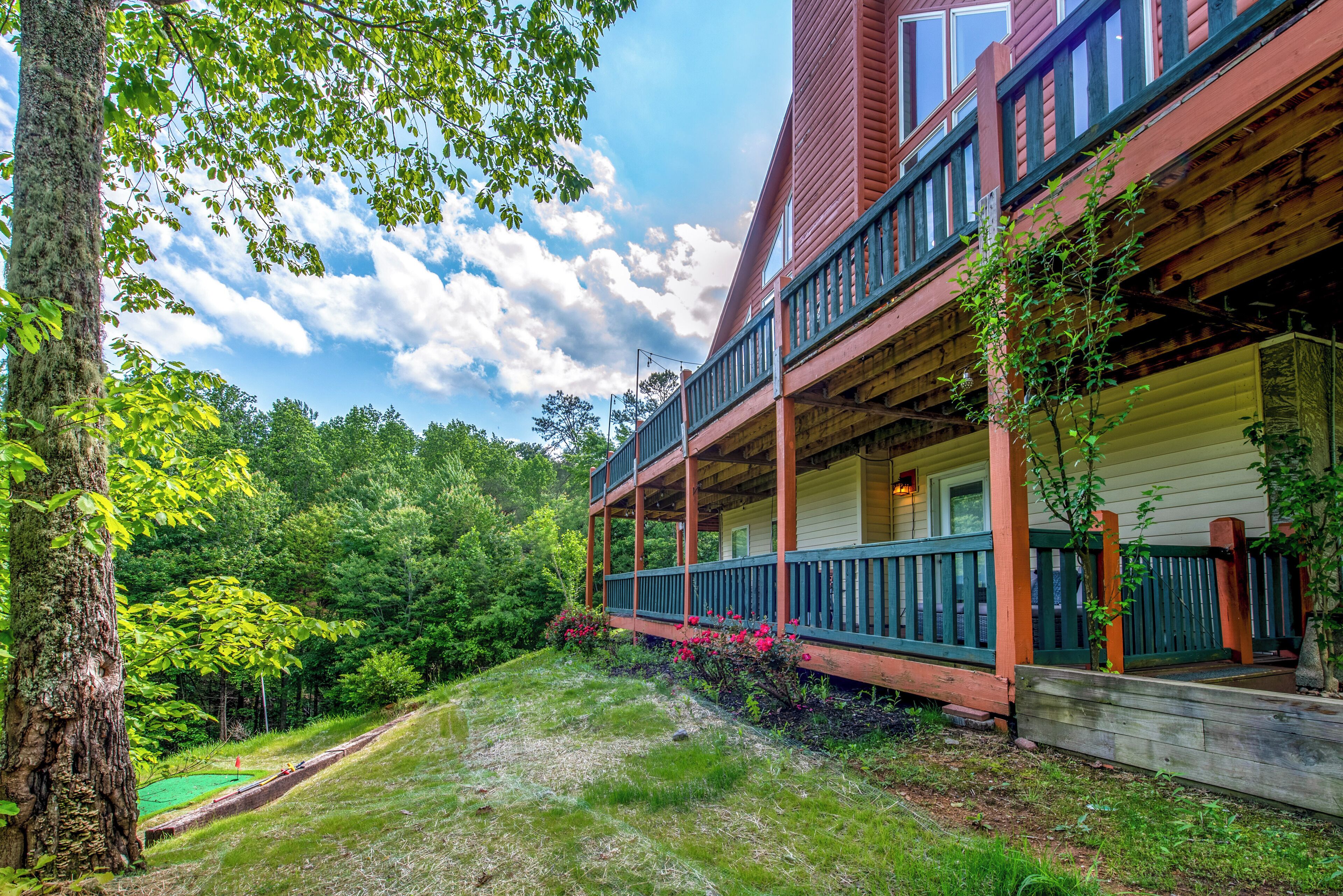 A two-story cabin with a porch, surrounded by lush greenery and a clear sky.