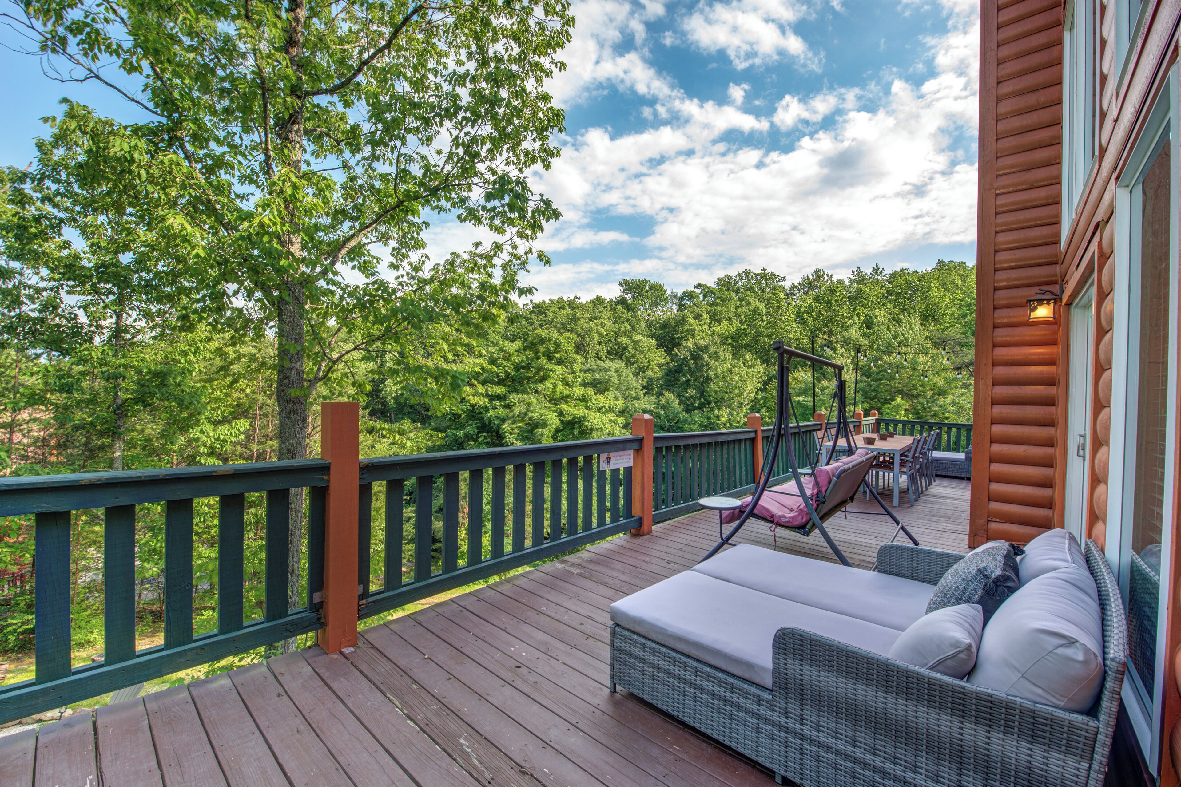 A wooden deck with outdoor furniture, a railing, and a view of a forested area.
