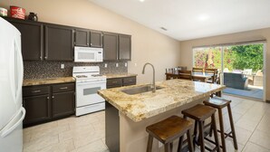 Una cocina con armarios oscuros, estufa blanca, microondas e isla con encimera de granito y pileta.
