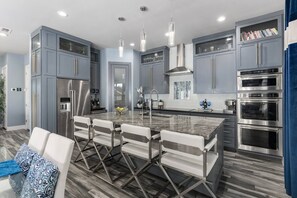 A modern kitchen with grey cabinets, stainless steel appliances, and a marble island with seating.