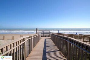 Ein Holzsteg führt zu einem Strand mit Blick auf den Ozean.