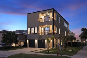 A modern two-story residential building with a balcony on the upper floor, large windows, and a well-maintained lawn.