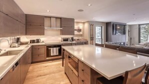 A modern kitchen with a large island, built-in appliances, and a dining area with a large table. - Luxury Ski-In/Out Residence at Golden Peak (Vail)