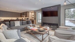A modern living room with a grey sofa, a coffee table, and a fireplace. - Luxury Ski-In/Out Residence at Golden Peak (Vail)