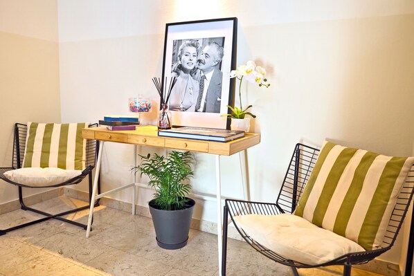 A room with two striped chairs, a small desk with a framed photo, a potted plant, and a vase with flowers. - Leone sea view apartments on the Rimini seafront (Rimini)