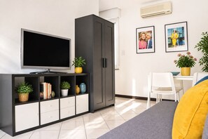 A modern living room with a flat-screen TV, a grey cabinet with shelves, a dining area with a white table and chairs, and two framed pictures on the wall. - Leone sea view apartments on the Rimini seafront (Rimini)