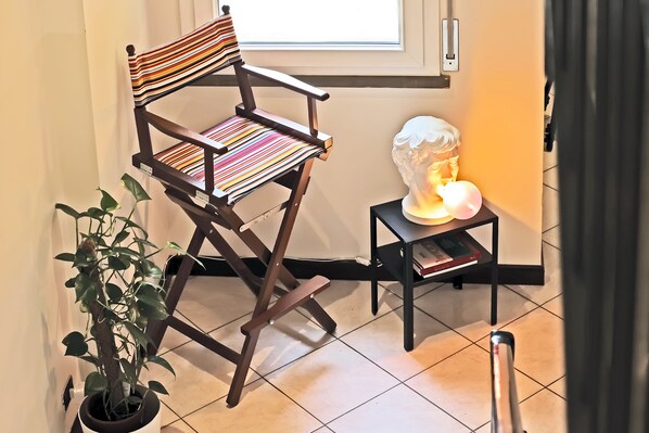 Une chaise en bois avec un coussin à rayures, une plante en pot et un buste sculpté posé sur une petite table.