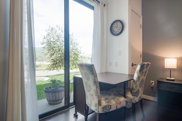 A dining area with a table and chairs, a clock on the wall, and a view of the outdoors.