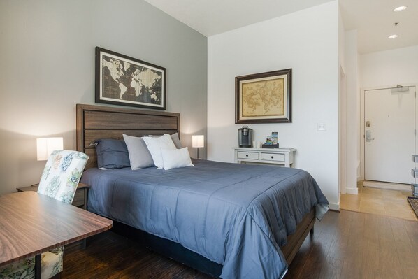 Un dormitorio ordenado con una cama grande, una mesita de noche, una silla y dos lámparas fijadas a la pared.