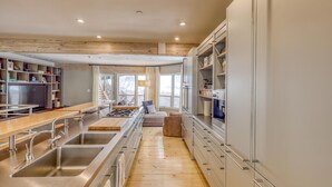A modern kitchen with a central island, built-in shelves, and a dining area with a long table. - Modern Vail Village Ski-in Ski-Out Townhome (Vail)