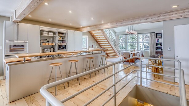 A modern kitchen with a central island, bar stools, and a staircase leading to an upper level. - Modern Vail Village Ski-in Ski-Out Townhome (Vail)
