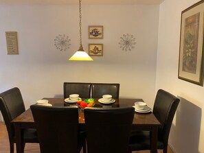 A dining area with a table for four, illuminated by a pendant light, surrounded by artwork and decorative wall hangings.